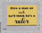 A taped needlepoint canvas with the design: Give a Man an Inch.